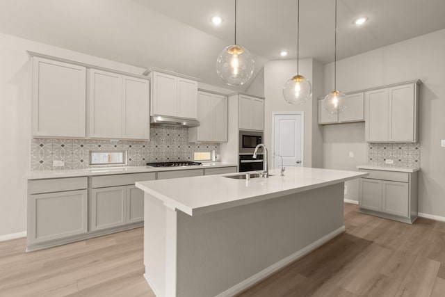 kitchen with stainless steel appliances, sink, a kitchen island with sink, and light hardwood / wood-style flooring