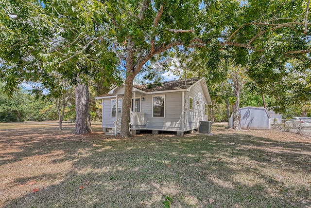 rear view of property featuring central AC, a storage shed, and a yard