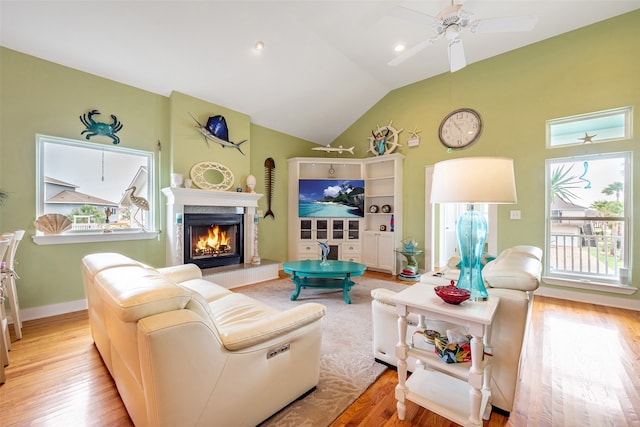 living room with a tiled fireplace, a ceiling fan, vaulted ceiling, wood finished floors, and baseboards