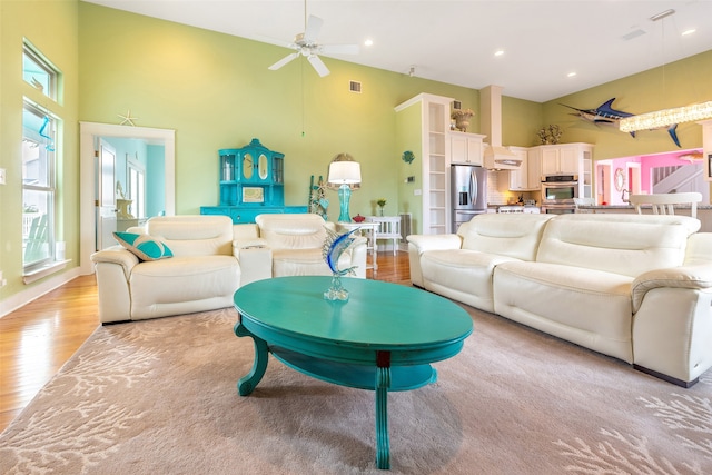 living area featuring light wood finished floors, visible vents, a towering ceiling, ceiling fan, and recessed lighting