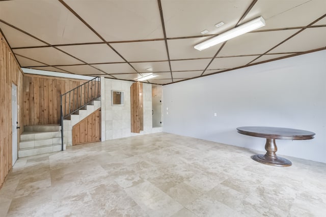 basement with a paneled ceiling, tile patterned flooring, and wooden walls