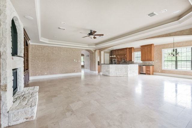 unfurnished living room featuring a stone fireplace, ceiling fan with notable chandelier, a tray ceiling, and light tile patterned floors