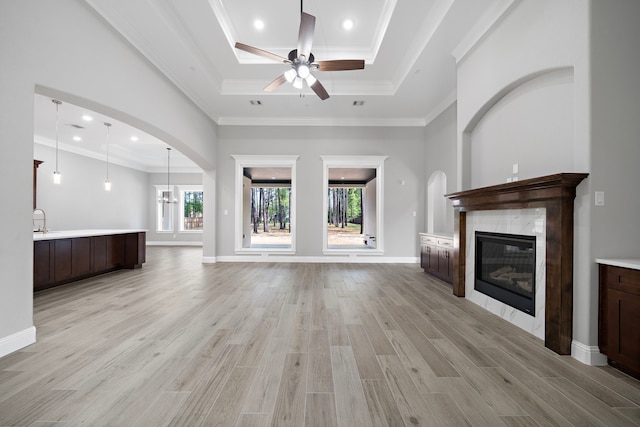 unfurnished living room featuring a raised ceiling, a fireplace, ceiling fan with notable chandelier, and ornamental molding