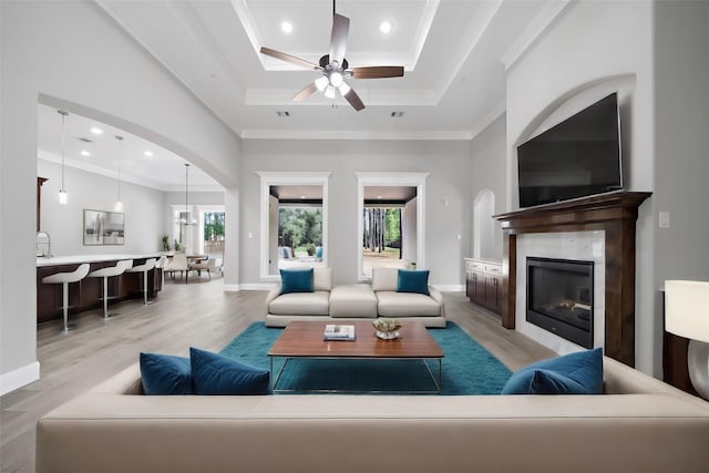 living room with ceiling fan, sink, crown molding, light hardwood / wood-style floors, and a tray ceiling