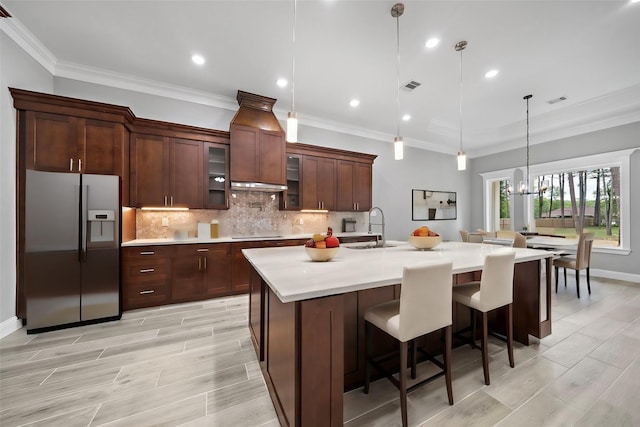 kitchen with sink, stainless steel refrigerator with ice dispenser, pendant lighting, a kitchen island with sink, and black electric stovetop