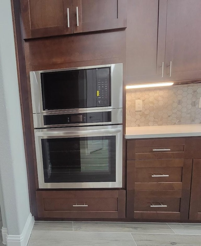 kitchen featuring built in microwave, decorative backsplash, stainless steel oven, and dark brown cabinets