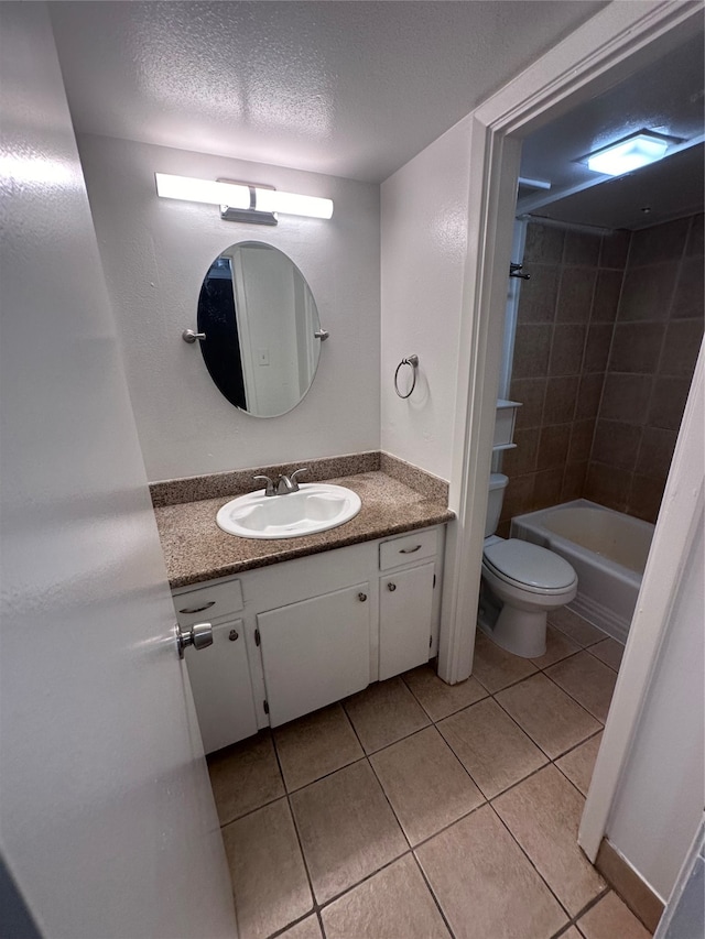 full bathroom featuring tiled shower / bath, tile floors, vanity, toilet, and a textured ceiling