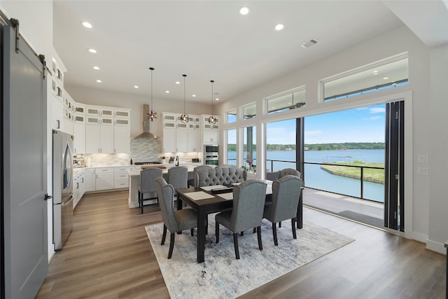 dining space with recessed lighting, visible vents, a water view, a barn door, and wood finished floors