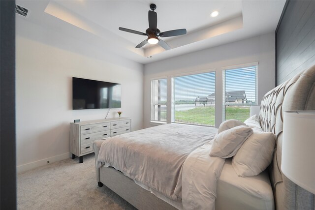 bedroom with light carpet, a tray ceiling, visible vents, and baseboards