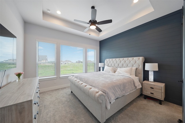 bedroom featuring a raised ceiling, light carpet, ceiling fan, and baseboards