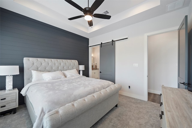 carpeted bedroom featuring a barn door, visible vents, a raised ceiling, and baseboards