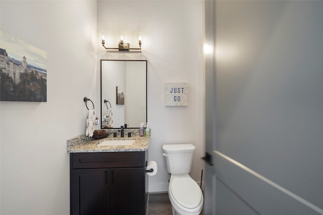 half bath featuring baseboards, vanity, toilet, and wood finished floors