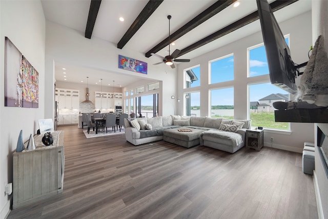 living room with a towering ceiling, a wealth of natural light, beam ceiling, and wood finished floors