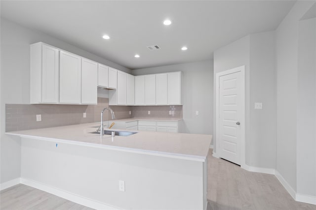 kitchen with white cabinets, kitchen peninsula, sink, tasteful backsplash, and light wood-type flooring