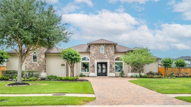 view of front of house featuring french doors, decorative driveway, stucco siding, stone siding, and a front lawn