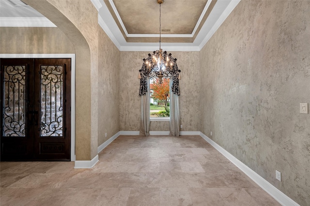 entryway with a notable chandelier, a raised ceiling, crown molding, and french doors