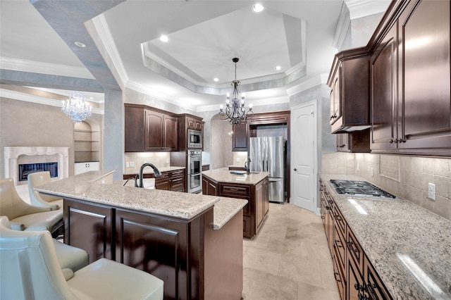 kitchen with a breakfast bar, a kitchen island with sink, appliances with stainless steel finishes, a tray ceiling, and decorative light fixtures