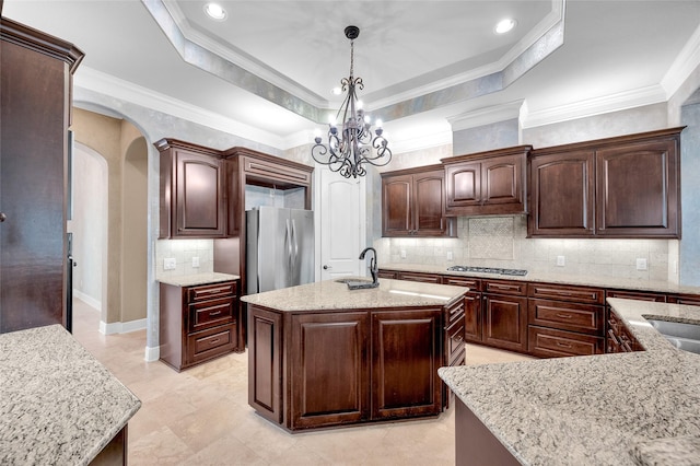 kitchen featuring pendant lighting, a raised ceiling, a kitchen island with sink, and appliances with stainless steel finishes