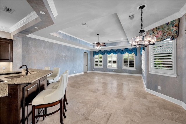 dining space with a raised ceiling, a wealth of natural light, sink, and ceiling fan with notable chandelier