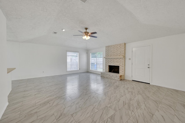 unfurnished living room with a fireplace, ceiling fan, light tile floors, and a textured ceiling