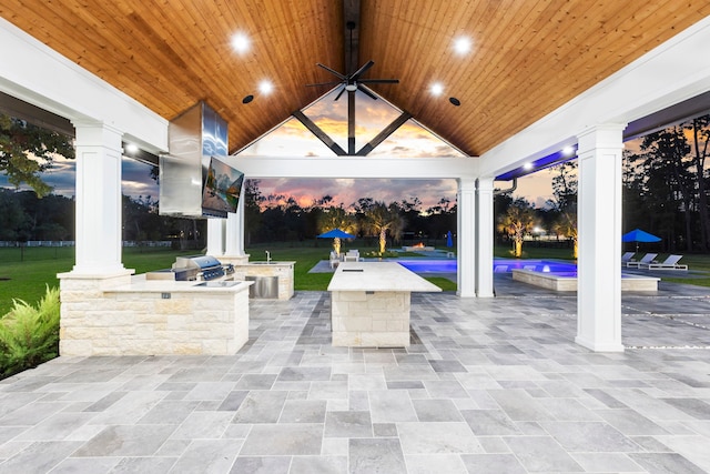 patio terrace at dusk featuring a grill, ceiling fan, and exterior kitchen