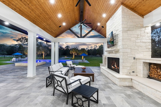 patio terrace at dusk featuring an outdoor stone fireplace and ceiling fan