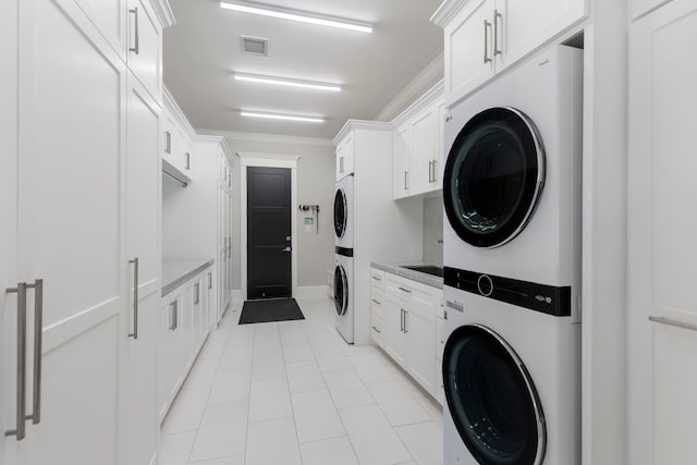 laundry area with cabinets, ornamental molding, stacked washer and dryer, and light tile floors