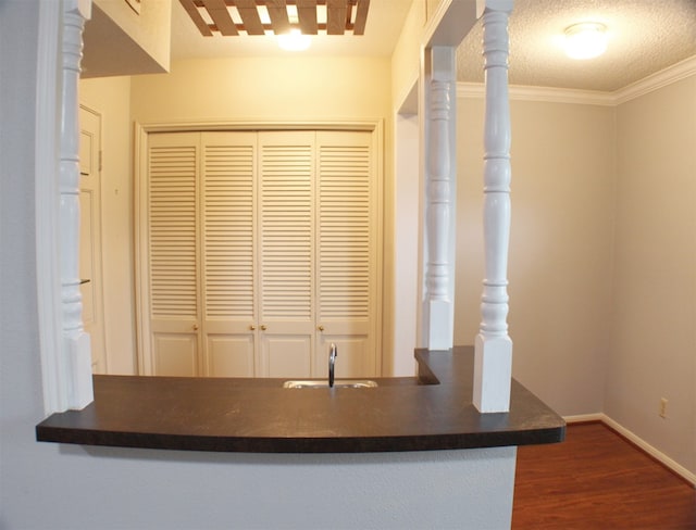 kitchen featuring dark hardwood / wood-style floors, ornamental molding, kitchen peninsula, sink, and a textured ceiling