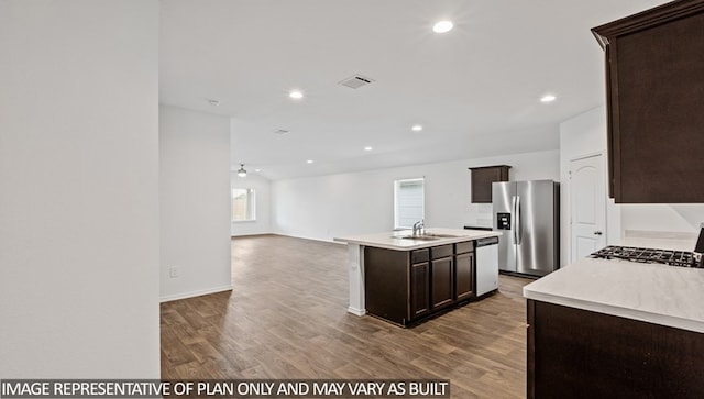 kitchen featuring a kitchen island with sink, ceiling fan, dark brown cabinets, wood-type flooring, and stainless steel appliances