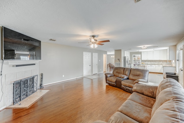 living room featuring a tile fireplace, ceiling fan, light wood-type flooring, and a textured ceiling