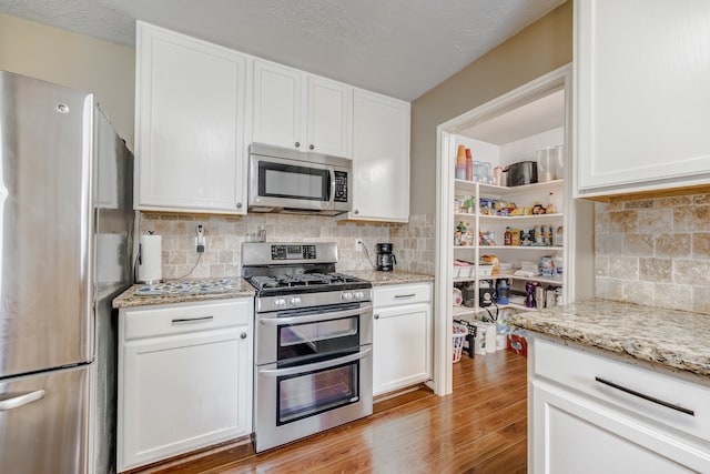 kitchen featuring appliances with stainless steel finishes, tasteful backsplash, light stone countertops, and light wood-type flooring