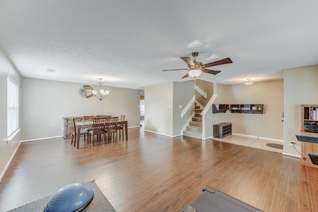 living room featuring ceiling fan with notable chandelier and light hardwood / wood-style flooring