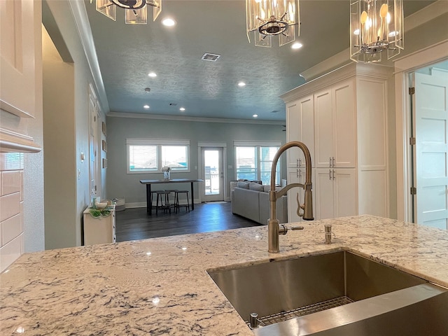 kitchen featuring sink, dark wood-type flooring, ornamental molding, pendant lighting, and light stone countertops