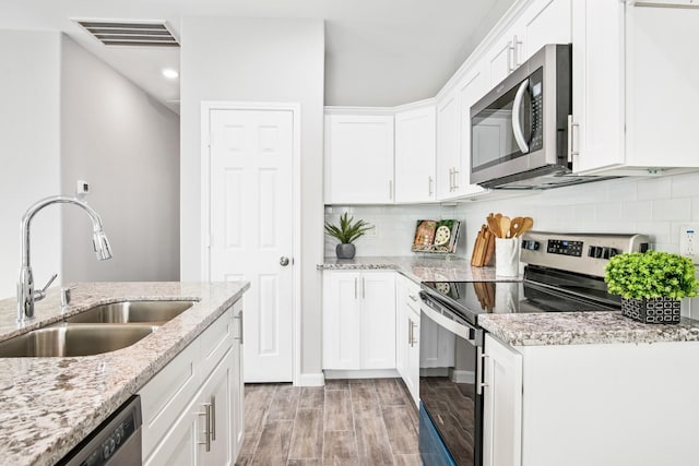 kitchen with white cabinetry, sink, light stone counters, light hardwood / wood-style flooring, and appliances with stainless steel finishes