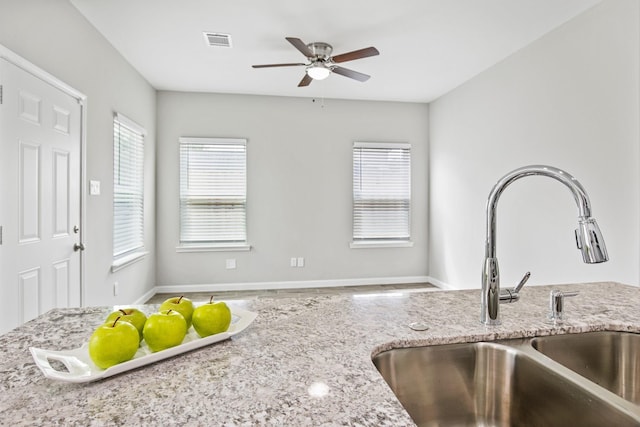 kitchen featuring ceiling fan, light stone counters, and sink