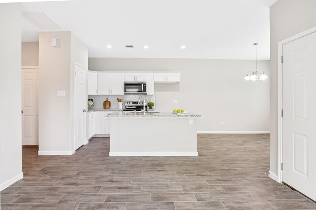 kitchen featuring appliances with stainless steel finishes, light stone counters, a kitchen island with sink, decorative light fixtures, and white cabinets