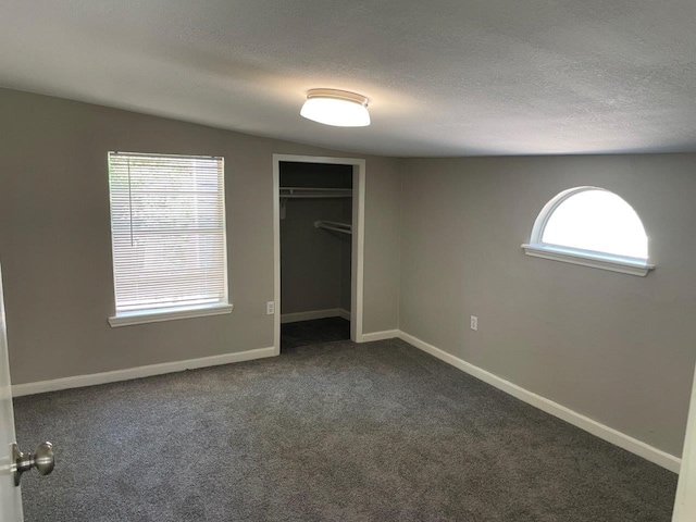 unfurnished bedroom featuring multiple windows, dark carpet, and a closet