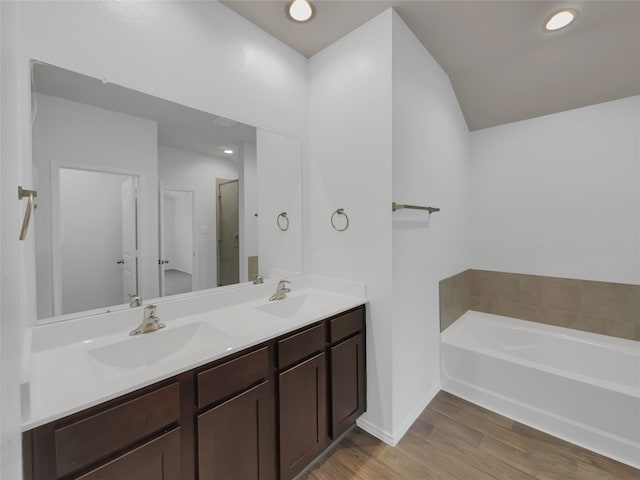 bathroom featuring a bath to relax in, double vanity, and wood-type flooring