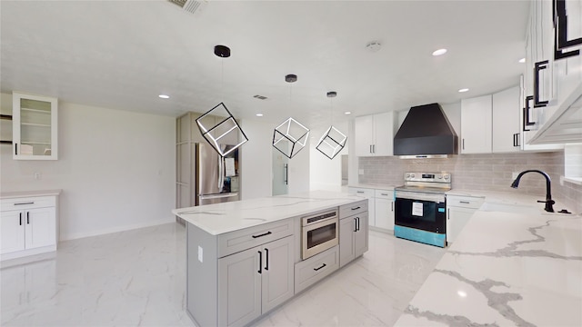 kitchen featuring wall chimney range hood, hanging light fixtures, appliances with stainless steel finishes, white cabinets, and light tile floors