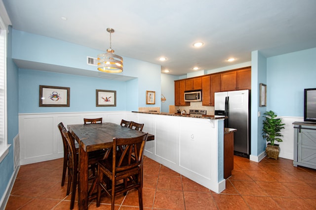 kitchen featuring kitchen peninsula, stone countertops, stainless steel appliances, tile flooring, and pendant lighting