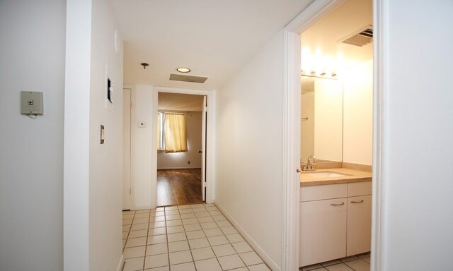 hallway featuring light tile patterned flooring, visible vents, a sink, and baseboards