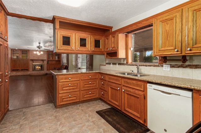 kitchen with ceiling fan, kitchen peninsula, a brick fireplace, dishwasher, and light stone countertops