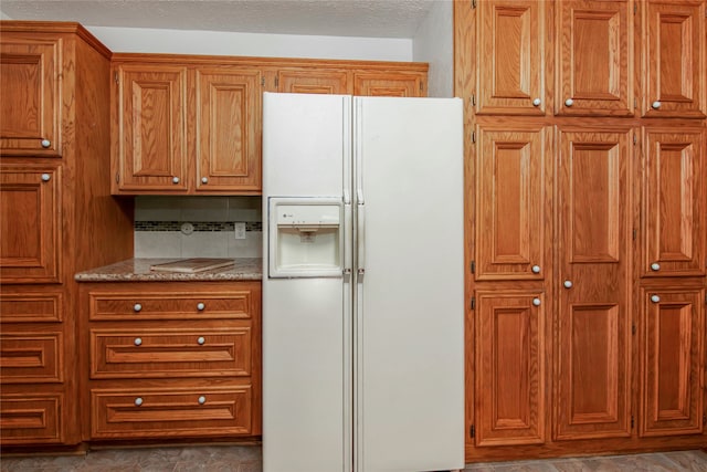 kitchen with decorative backsplash, a textured ceiling, white refrigerator with ice dispenser, and light stone countertops