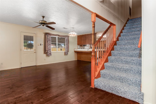 staircase with a textured ceiling, ceiling fan with notable chandelier, ornamental molding, and hardwood / wood-style floors