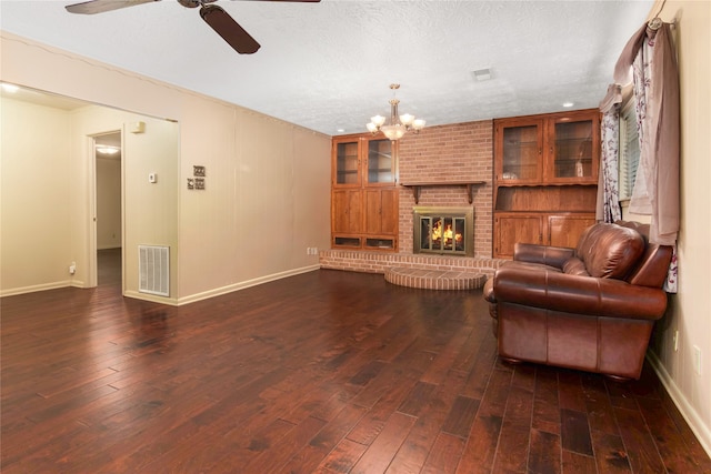 living room featuring ceiling fan with notable chandelier, a textured ceiling, a fireplace, and dark hardwood / wood-style flooring