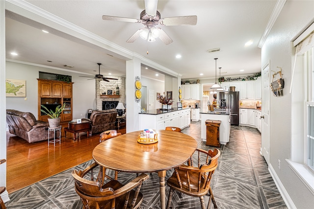 dining area featuring a fireplace, ornamental molding, hardwood / wood-style floors, and ceiling fan