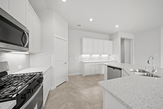 kitchen with white cabinets, stainless steel appliances, light stone counters, and sink