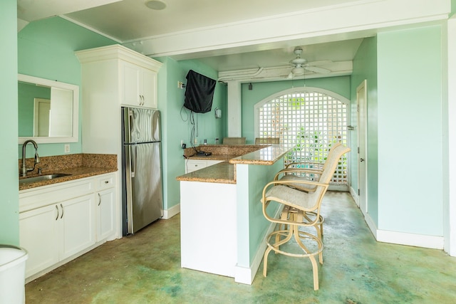 kitchen with a kitchen breakfast bar, stainless steel refrigerator, sink, dark stone counters, and ceiling fan