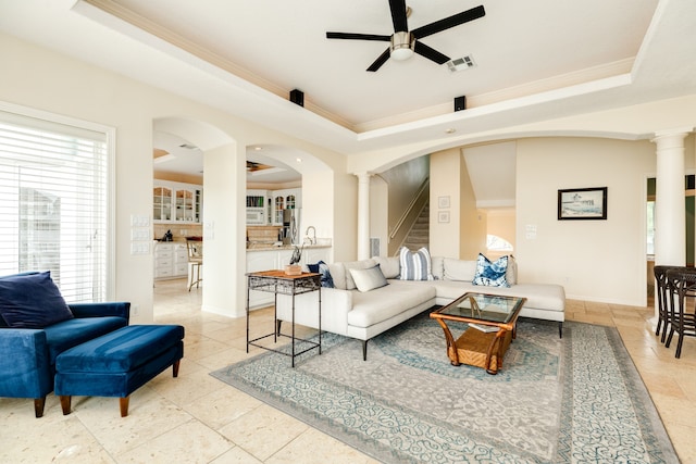 tiled living room with ceiling fan, crown molding, ornate columns, and a tray ceiling