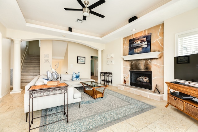 living room featuring a raised ceiling, ceiling fan, decorative columns, and a fireplace